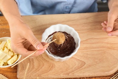 Young woman with cake pop and chocolate frosting at wooden table, above view