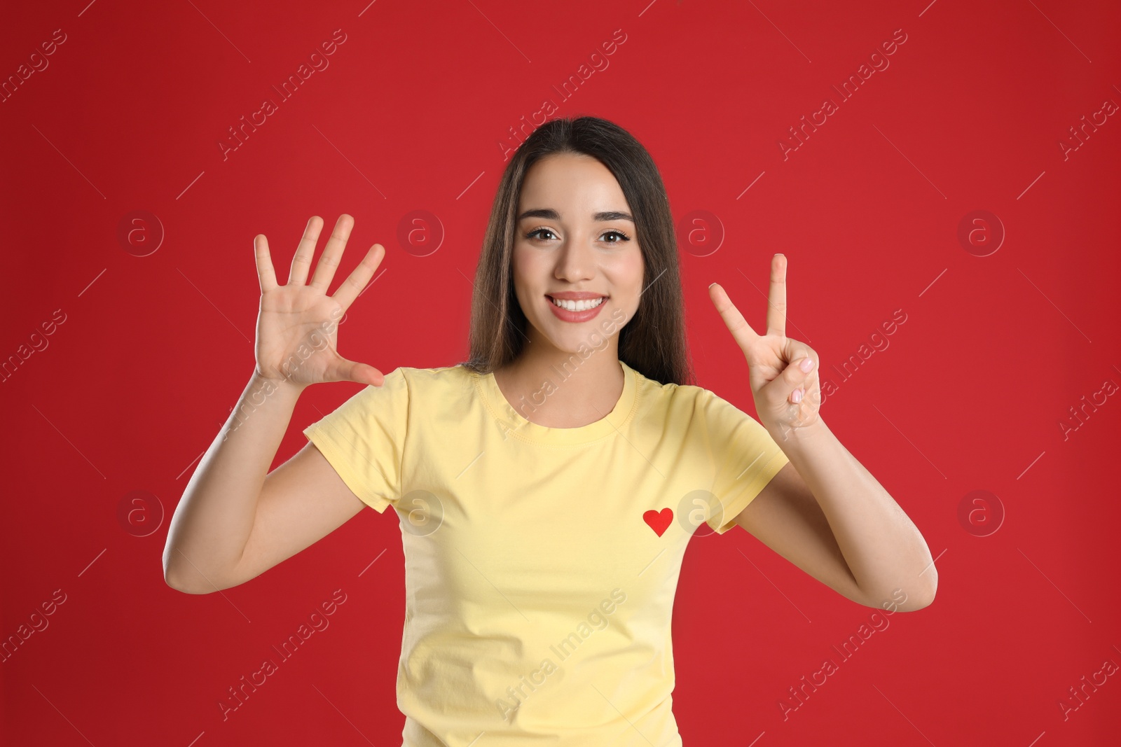 Photo of Woman in yellow t-shirt showing number seven with her hands on red background