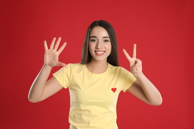 Photo of Woman in yellow t-shirt showing number seven with her hands on red background