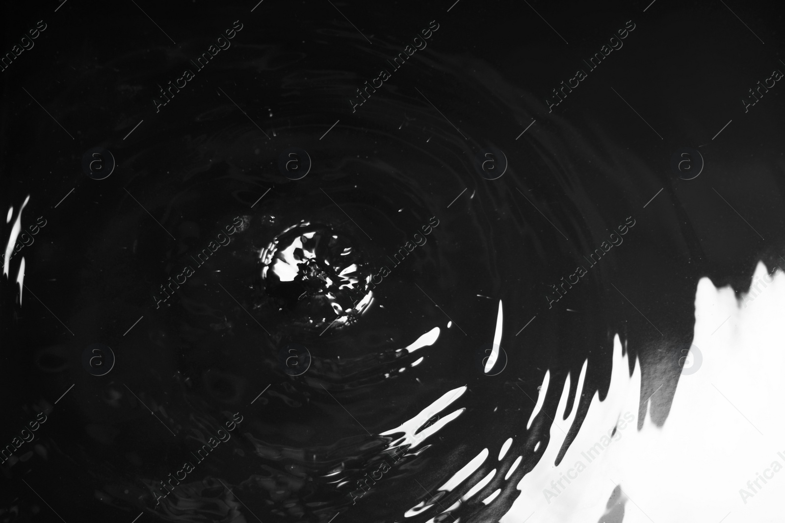 Photo of Rain drops falling down into puddle on dark background, closeup