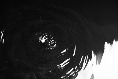 Photo of Rain drops falling down into puddle on dark background, closeup