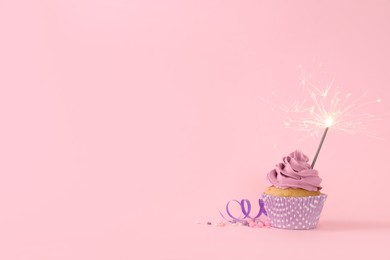 Photo of Birthday cupcake with burning sparkler, streamer and sprinkles on pink background. Space for text