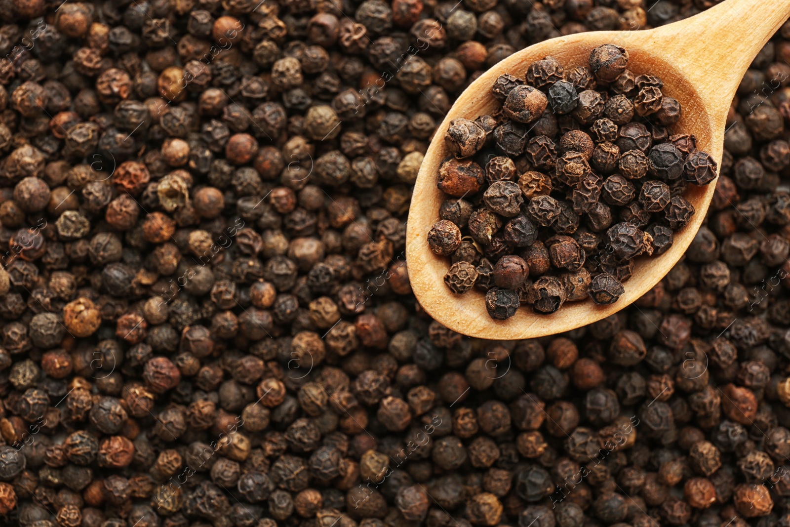 Photo of Spoon with black pepper over heap of grains, top view