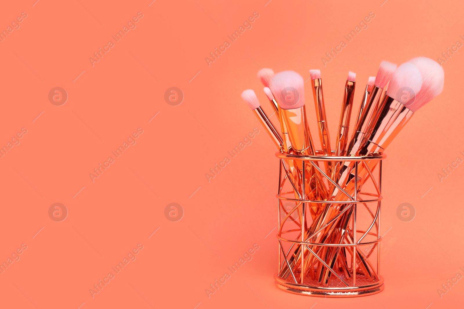 Photo of Set of makeup brushes in holder on coral background. Space for text