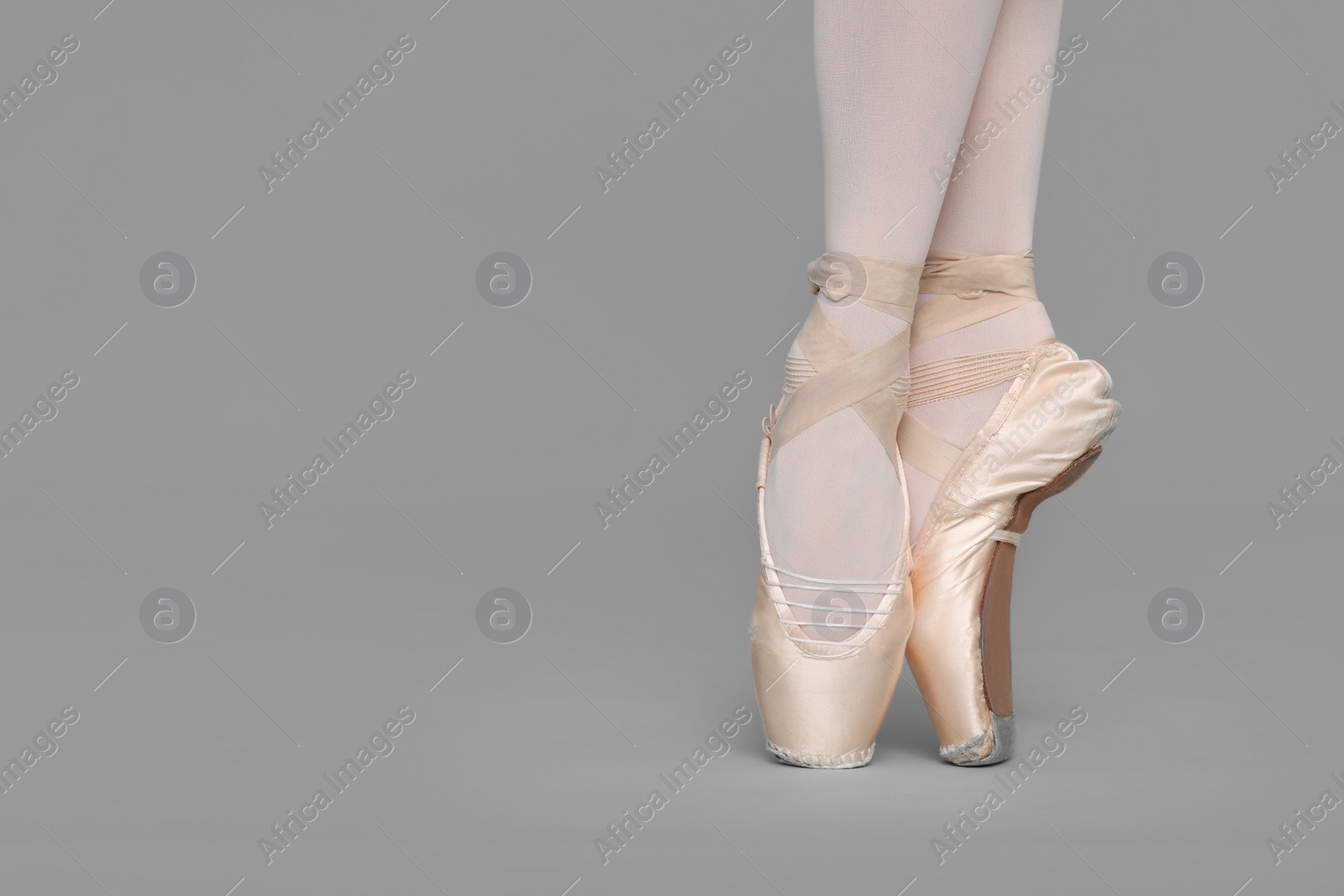 Photo of Young ballerina in pointe shoes practicing dance moves on grey background, closeup. Space for text