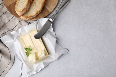 Tasty butter with curls, slices of bread and knife on light grey table, flat lay. Space for text