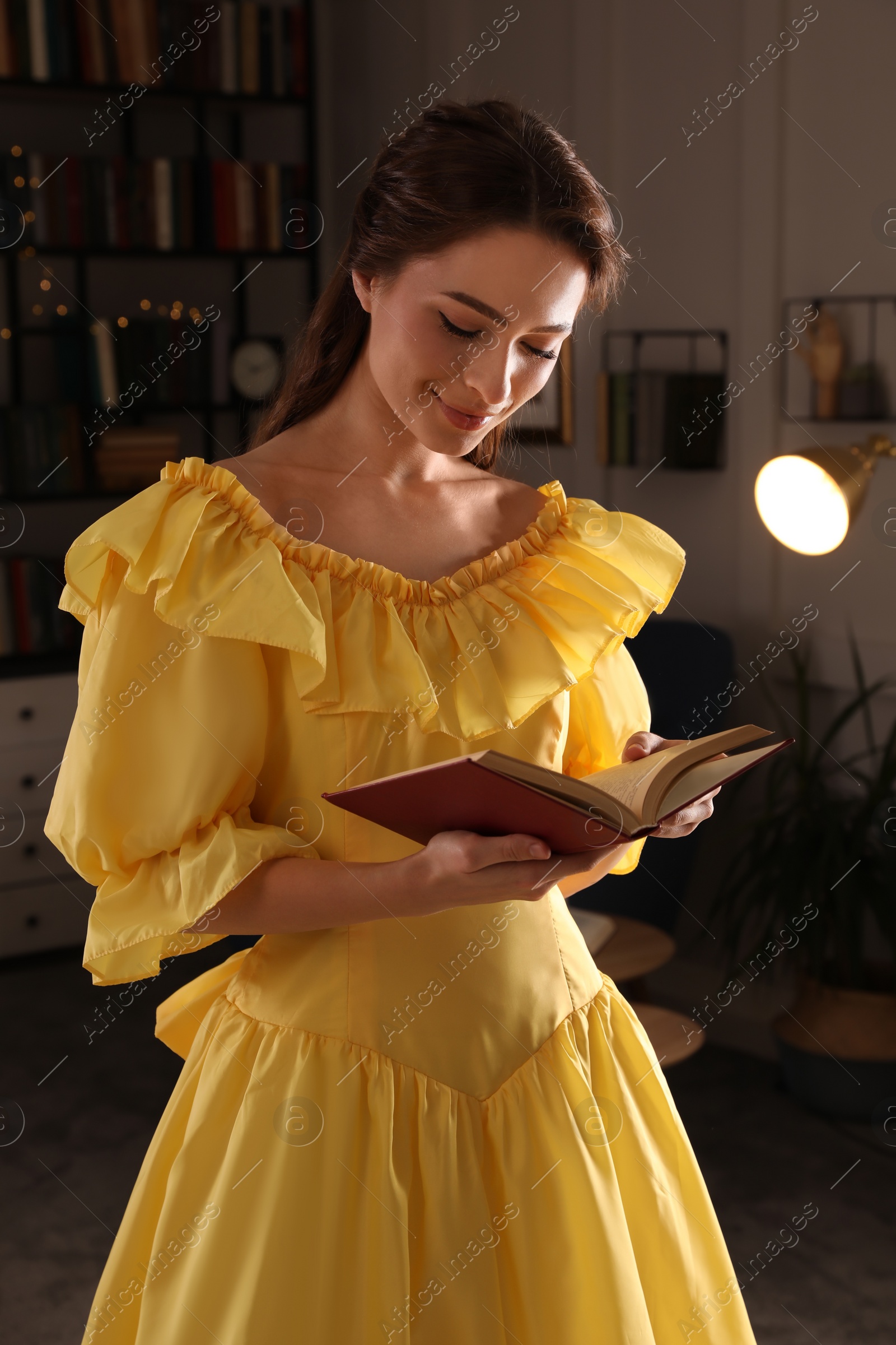 Photo of Beautiful young woman in yellow dress reading book at home