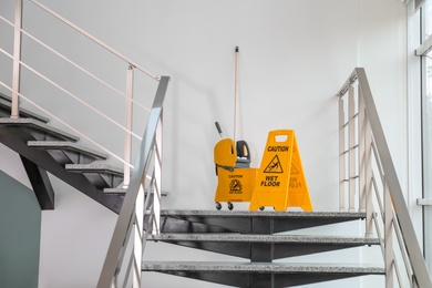 Photo of Safety sign with phrase Caution wet floor and mop bucket on stairs. Cleaning service