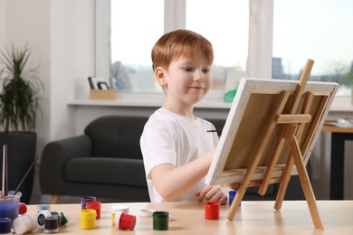 Little boy painting at table in studio. Using easel to hold canvas