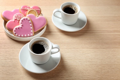 Photo of Romantic breakfast with heart shaped cookies and cups of coffee on wooden table, space for text