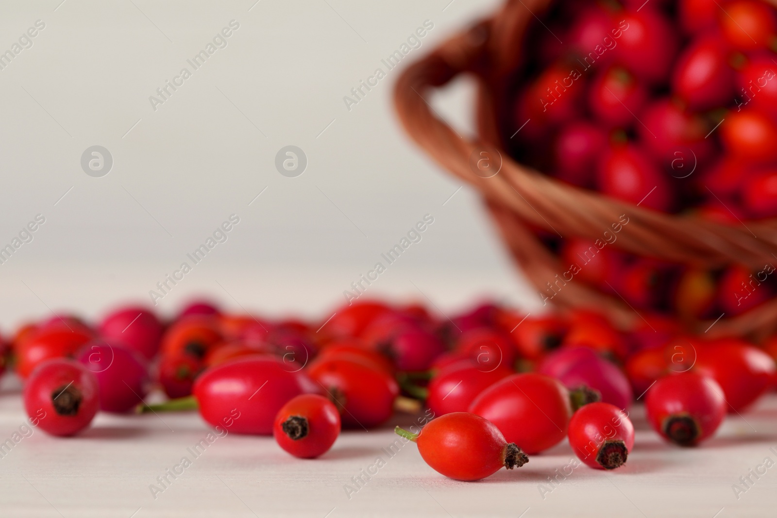 Photo of Ripe rose hip berries with wicker basket on white wooden table, closeup. Space for text