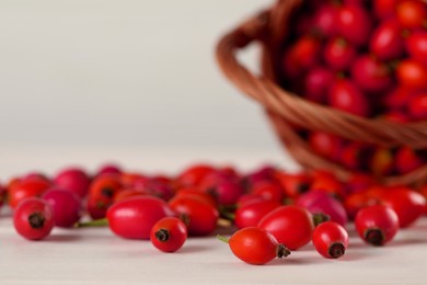 Photo of Ripe rose hip berries with wicker basket on white wooden table, closeup. Space for text