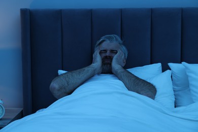 Photo of Mature man suffering from headache in bed at night