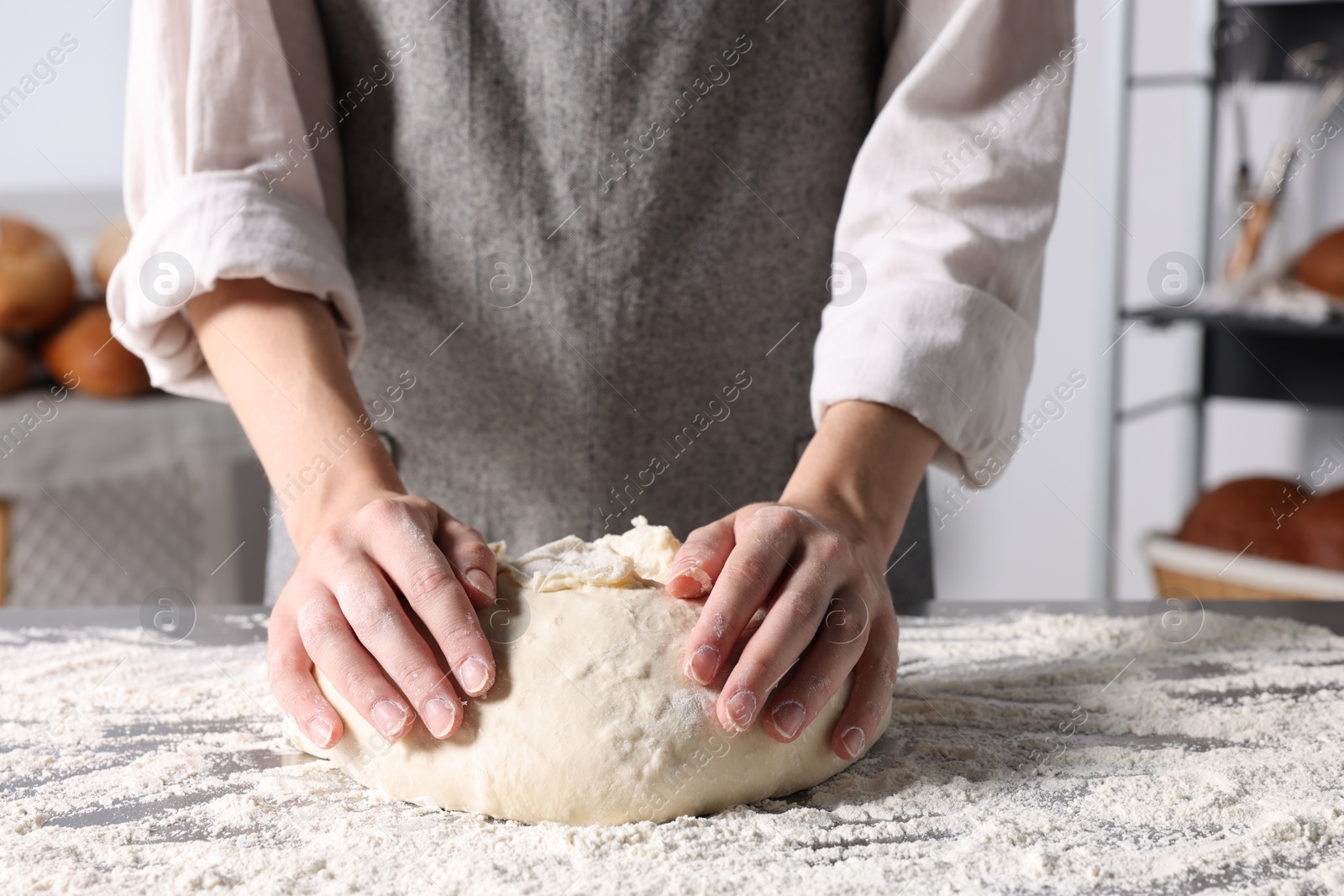 Photo of Woman kneading dough at table in kitchen, closeup