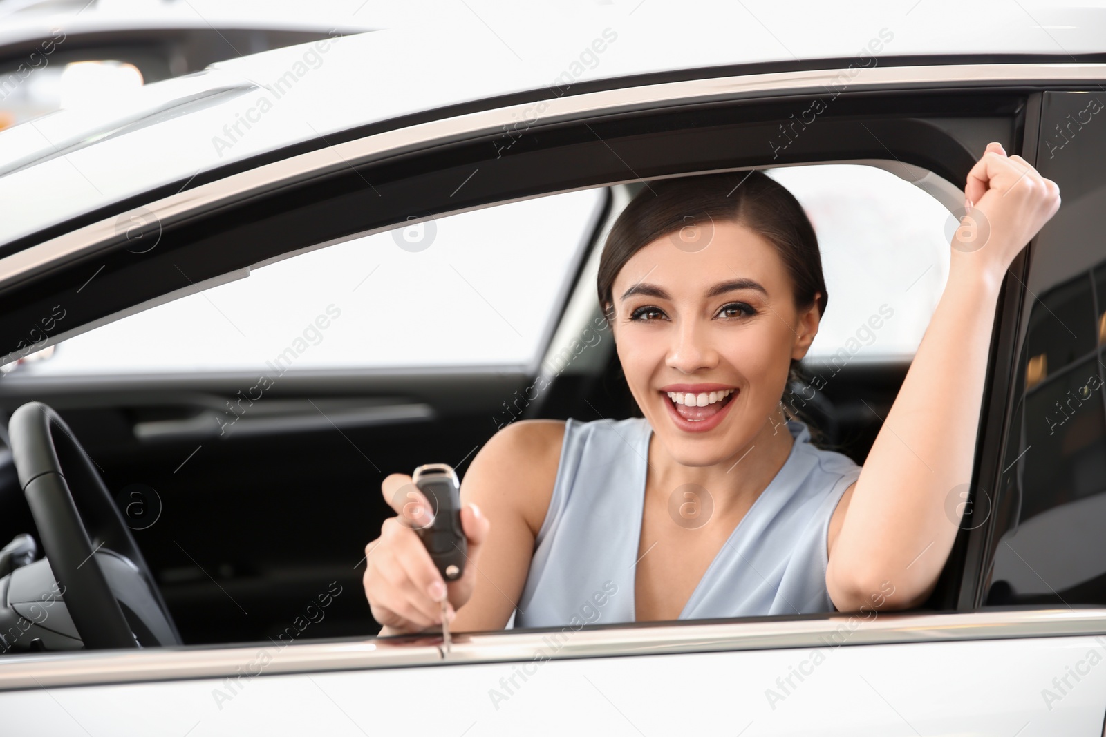 Photo of Young woman with key sitting in driver's seat of new car at salon