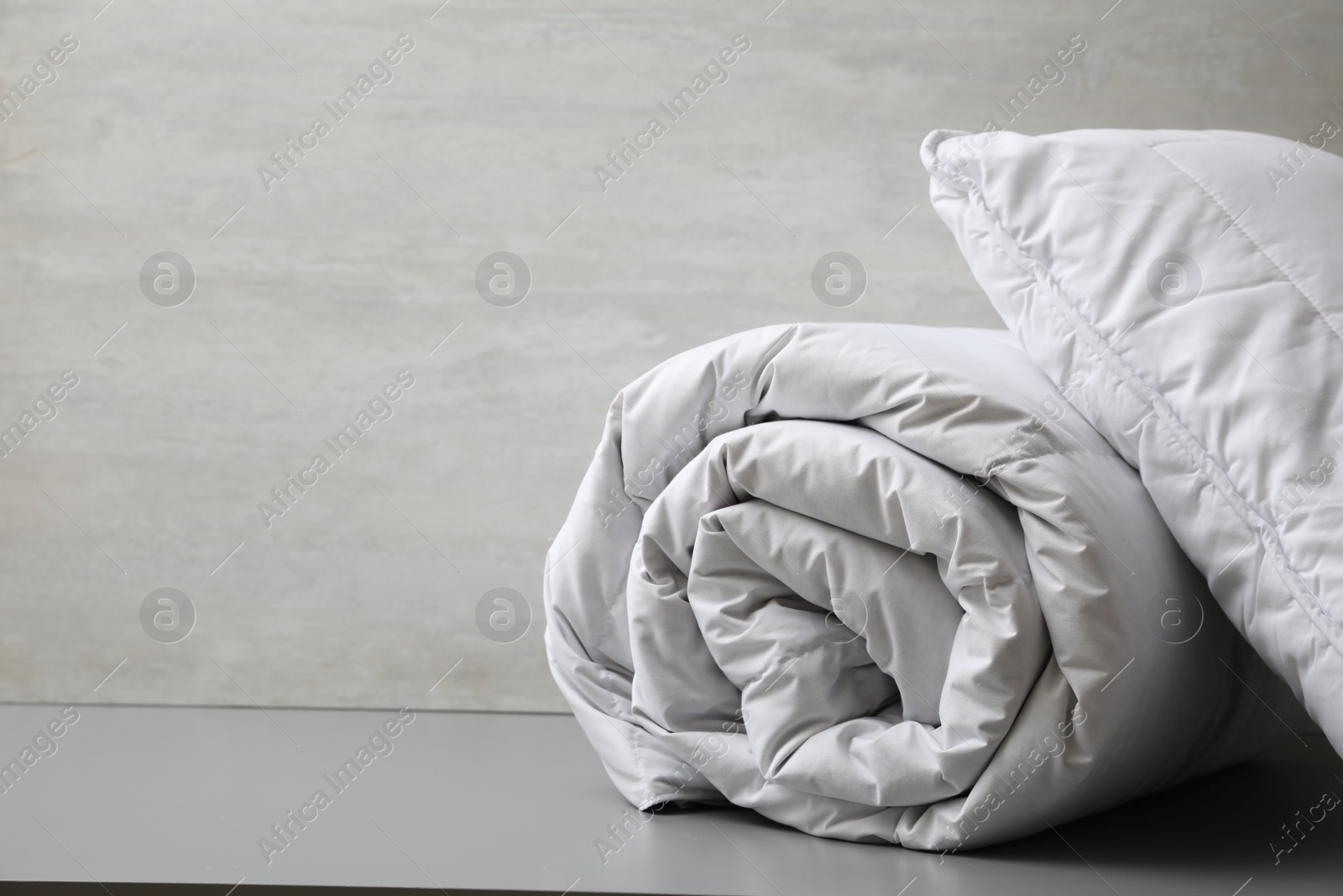 Photo of Soft blanket and pillow on light grey table, closeup. Space for text