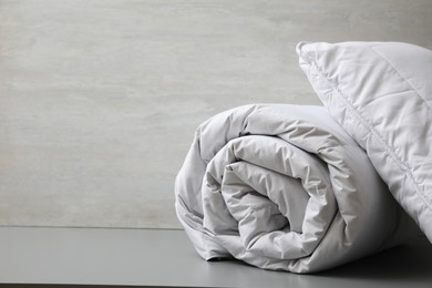 Photo of Soft blanket and pillow on light grey table, closeup. Space for text