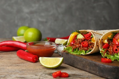 Board with delicious meat tortilla wraps on wooden table against grey background