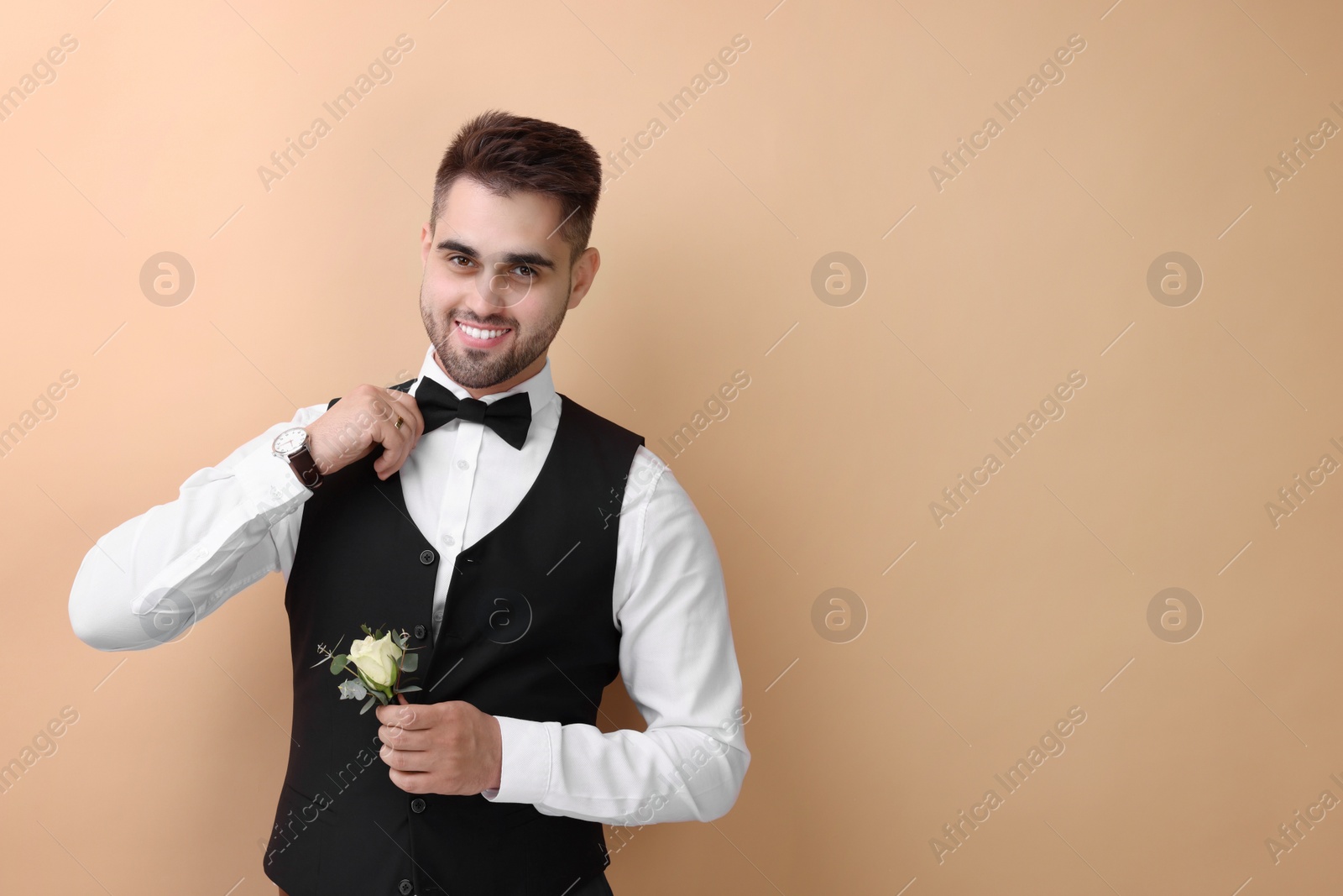 Photo of Handsome young groom with boutonniere on beige background, space for text. Wedding accessory