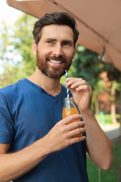 Photo of Handsome man with bottle of delicious juice outdoors