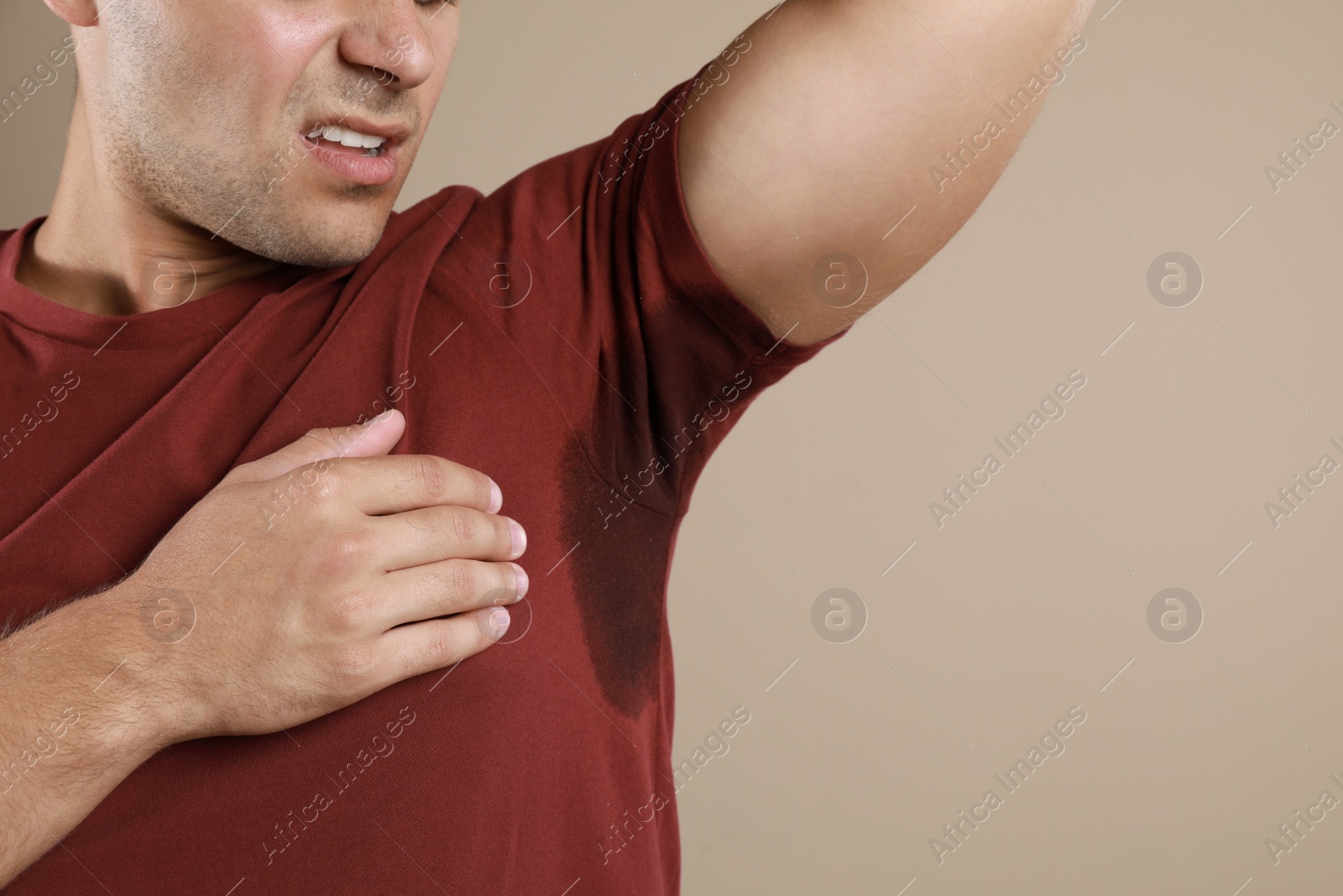 Photo of Young man with sweat stain on his clothes against beige background, closeup. Using deodorant