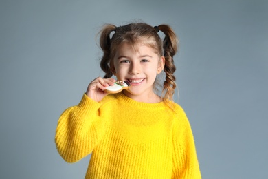 Cute little girl with Christmas gingerbread cookie on light grey background