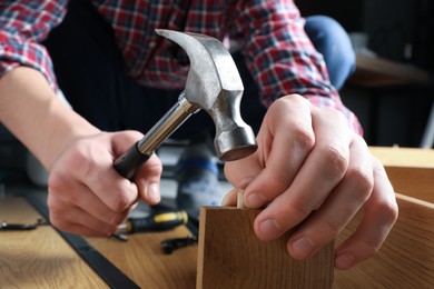 Photo of Man with hammer assembling wooden furniture indoors, closeup
