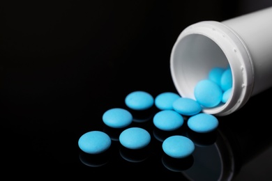 Photo of Container with blue pills on black background