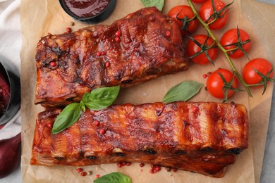 Photo of Tasty roasted pork ribs served with sauce, basil and tomatoes on table, top view