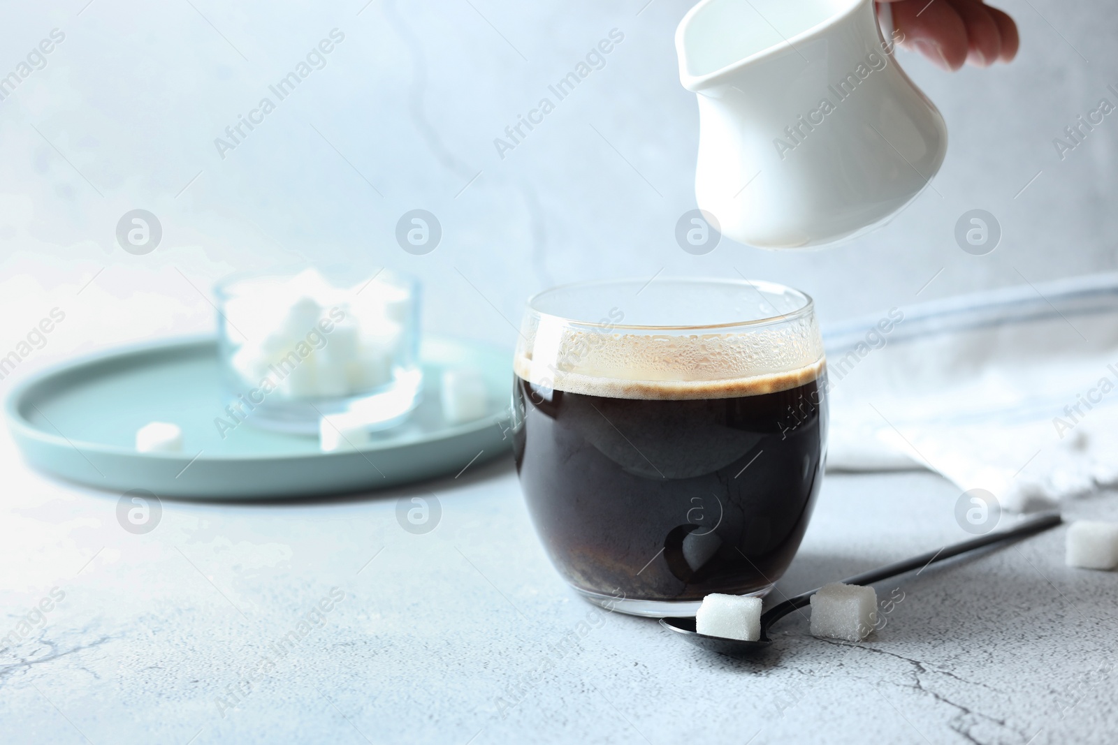 Photo of Pouring milk into cup with coffee on white textured table, closeup