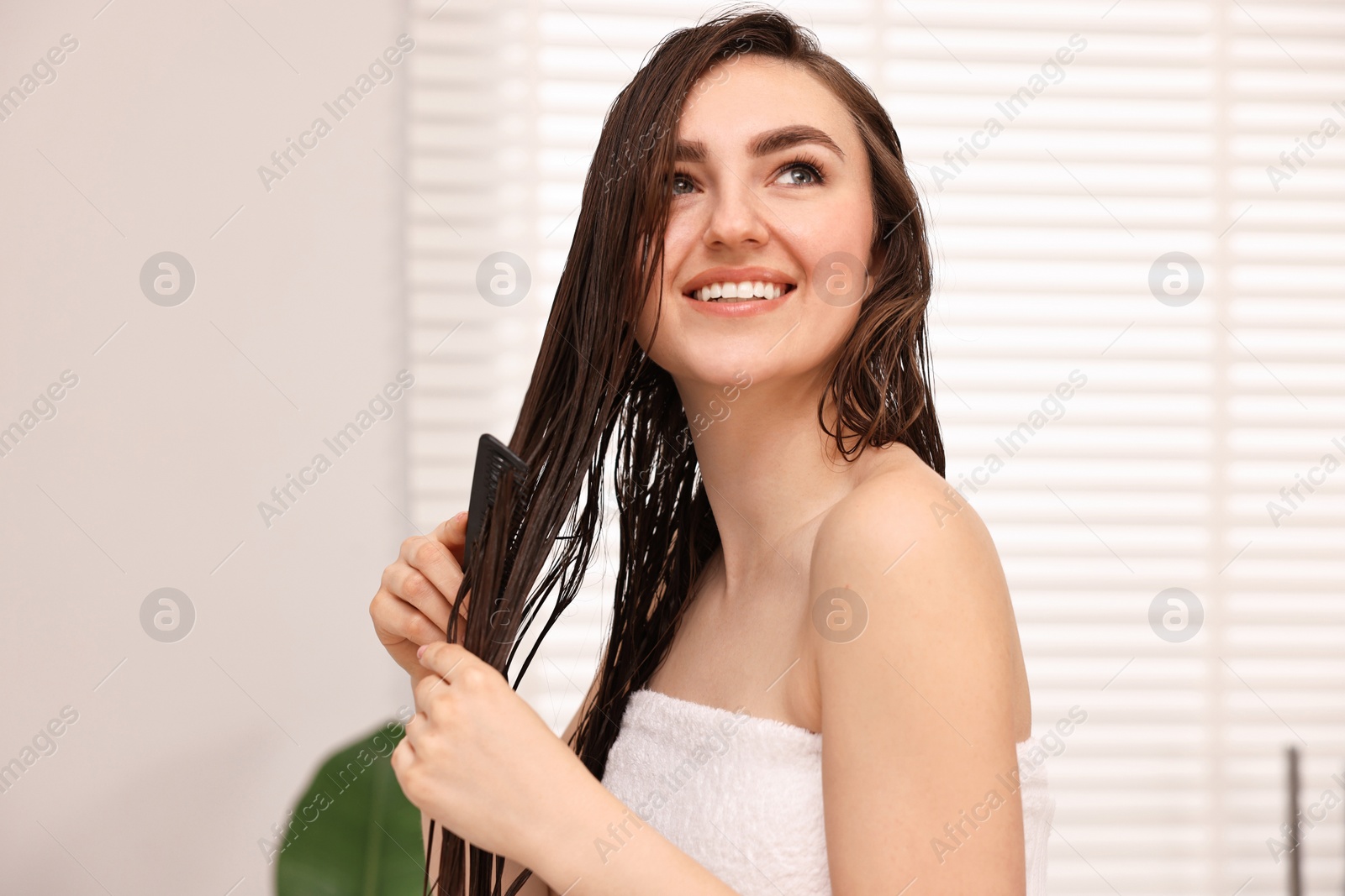 Photo of Young woman brushing hair after applying mask indoors