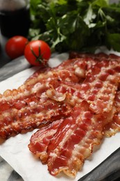 Photo of Fried bacon slices and tomatoes on marble board, closeup