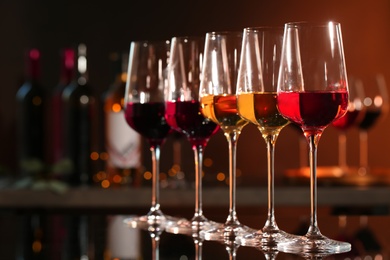 Photo of Row of glasses with different wines on bar counter against blurred background. Space for text