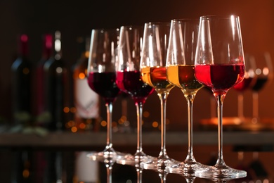 Row of glasses with different wines on bar counter against blurred background. Space for text