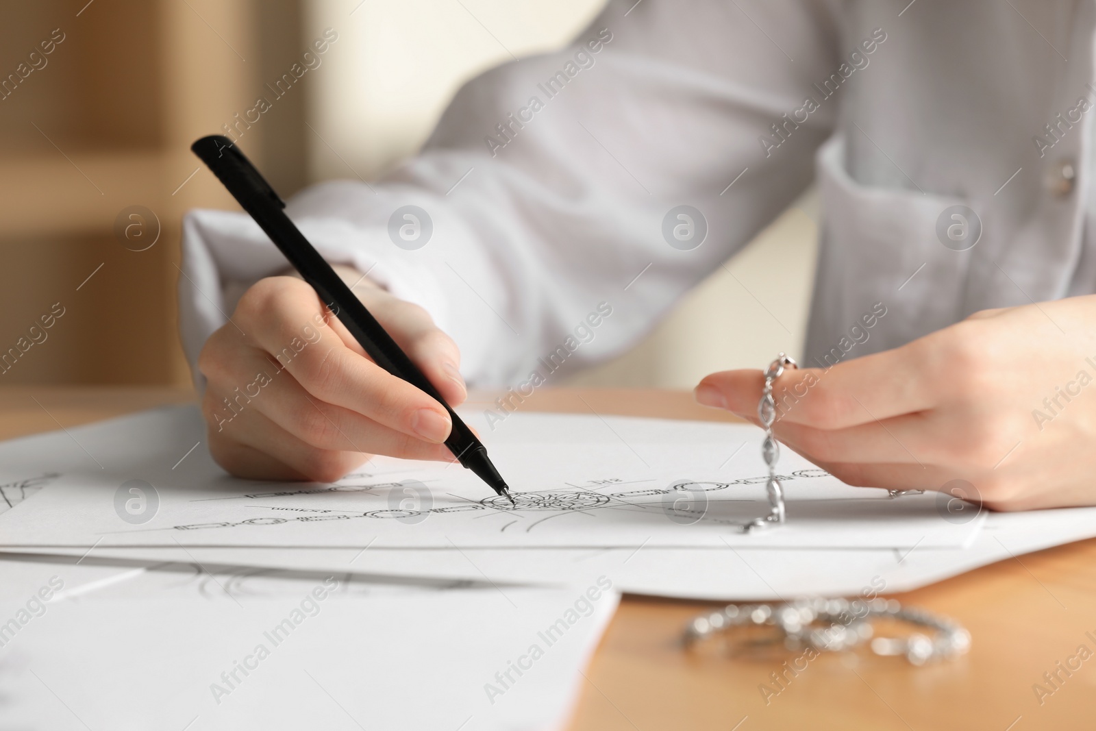 Photo of Jeweler drawing sketch of elegant bracelet on paper at wooden table indoors, closeup