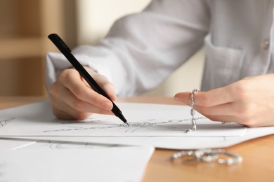 Photo of Jeweler drawing sketch of elegant bracelet on paper at wooden table indoors, closeup