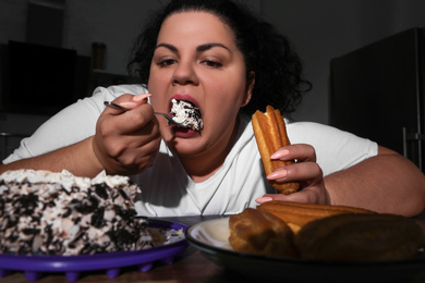 Photo of Depressed overweight woman eating sweets in kitchen at night