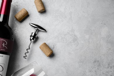 Photo of Corkscrew with wine bottle, glass and stoppers on light grey stone table, flat lay. Space for text