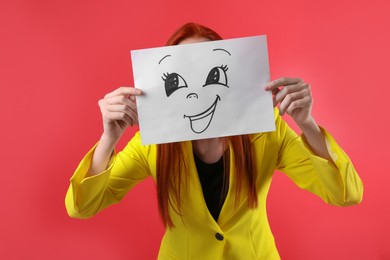 Woman hiding behind sheet of paper with happy face on red background