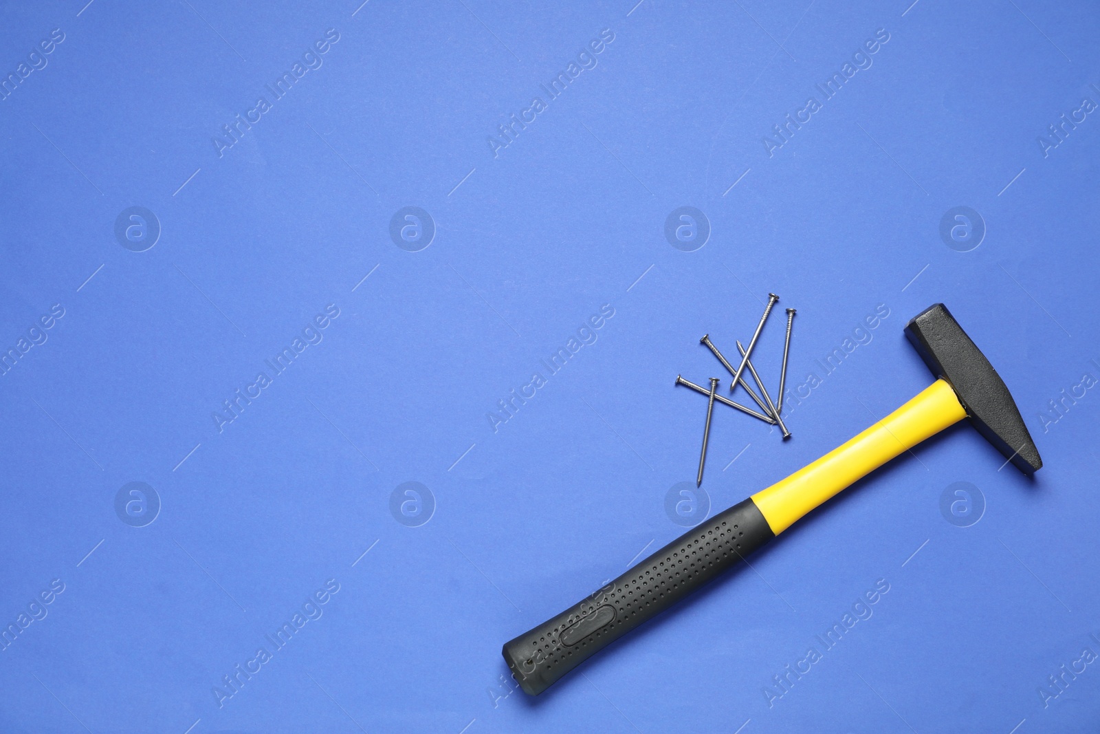 Photo of Hammer and metal nails on blue background, top view. Space for text