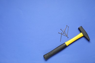 Hammer and metal nails on blue background, top view. Space for text