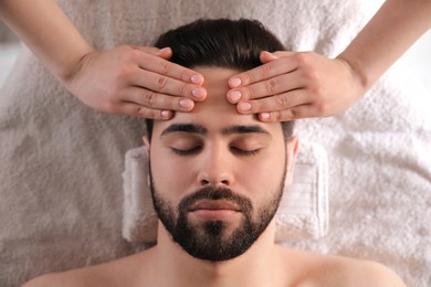 Photo of Young man receiving facial massage in beauty salon, top view