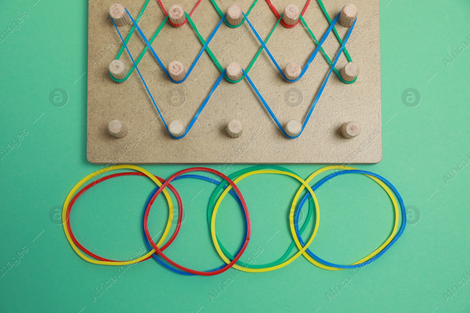 Photo of Wooden geoboard with rubber bands on green background, flat lay. Educational toy for motor skills development