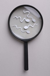 Photo of Reproductive medicine. Magnifier and sperm cells on gray background, top view