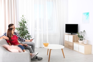 Photo of Happy young couple watching TV on sofa at home