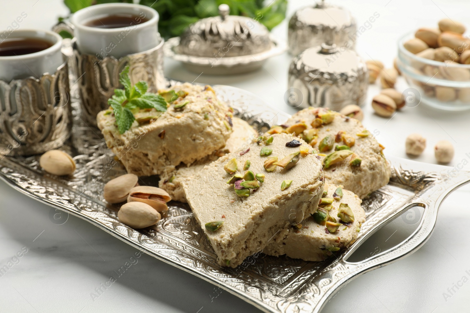 Photo of Tasty halva with pistachios and mint served on white table, closeup