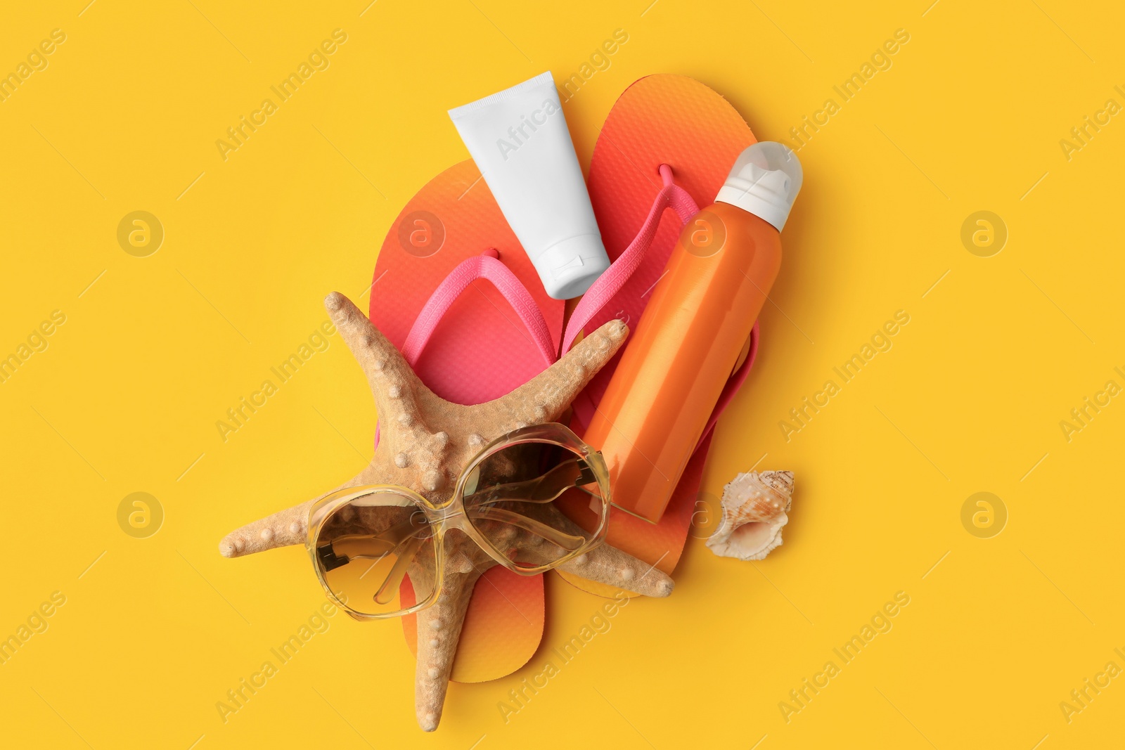 Photo of Sunscreen, sunglasses, starfish and flip flops on orange background, flat lay. Sun protection