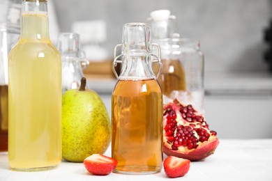 Tasty kombucha in glass bottles and fresh fruits on white tiled table