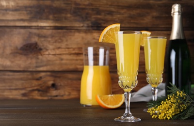 Photo of Glasses of Mimosa cocktail with garnish on wooden table. Space for text