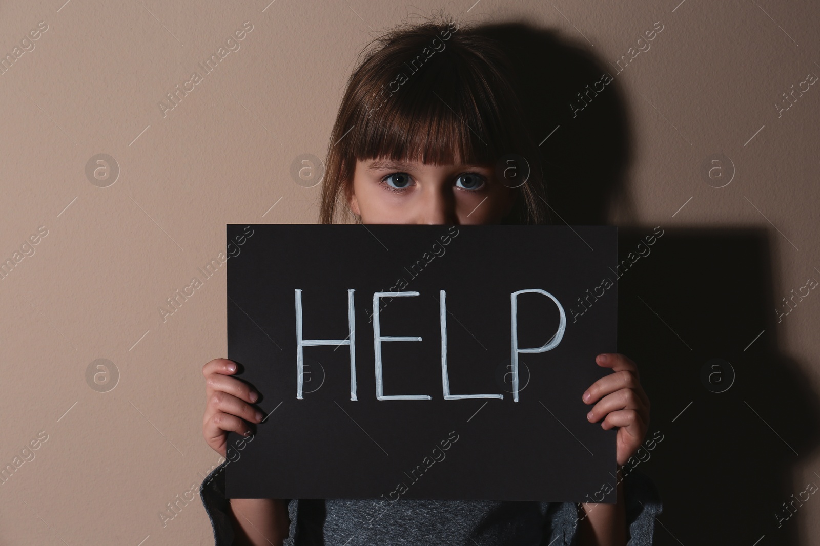 Photo of Abused little girl with sign HELP near beige wall. Domestic violence concept